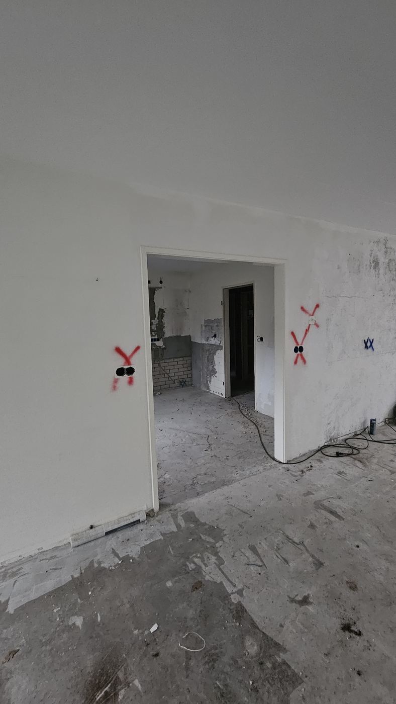 Witte muur met een smalle deuropening naar de keuken, met markeringen voor de doorbraak