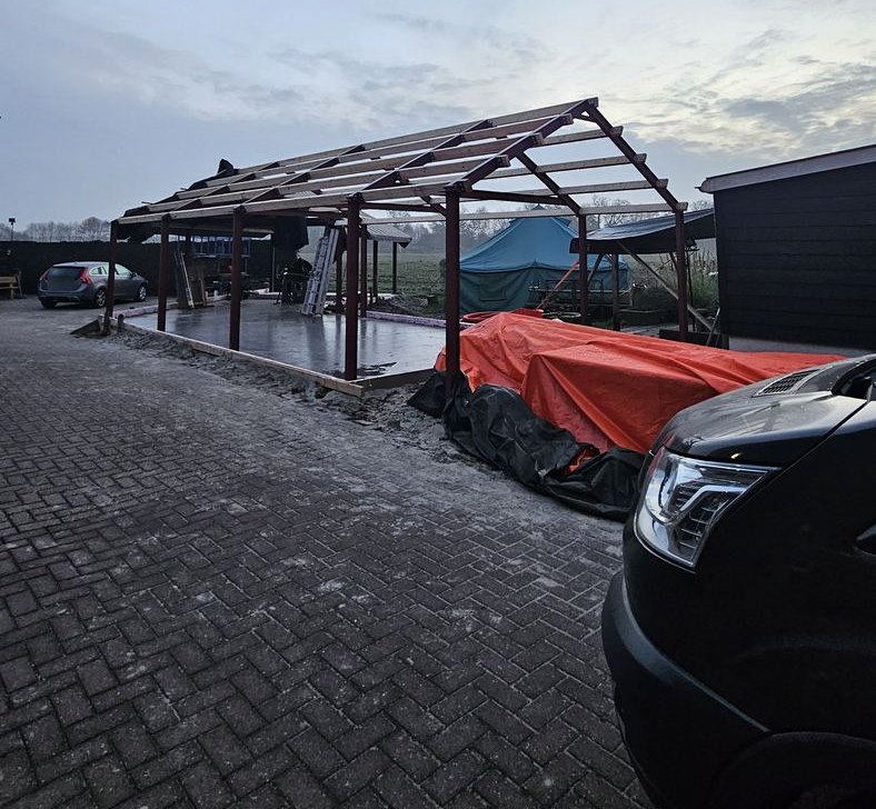 Rood geschilderde stalen spanten op een betonvloer met houten gordingen erop