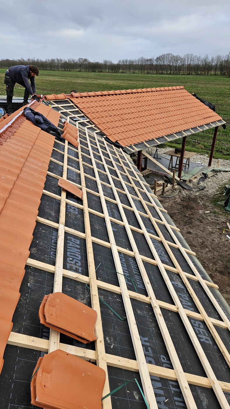 Dakvlak met zwarte dakfolie, tengels en panlatten, deels gedekt met oranje dakpannen
