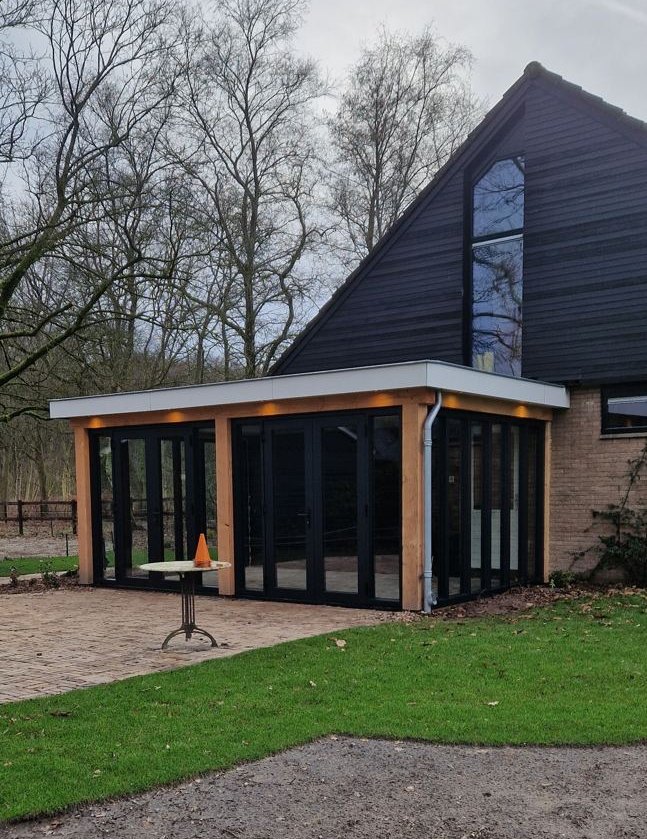 Tuinkamer met glazen pui naast de woning met houten gevel